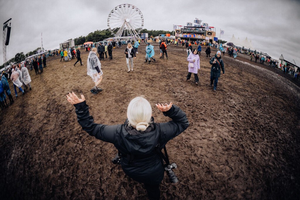 Person mit ausgebreiteten Armen steht im Schlamm und genießt die Festivalatmosphäre.