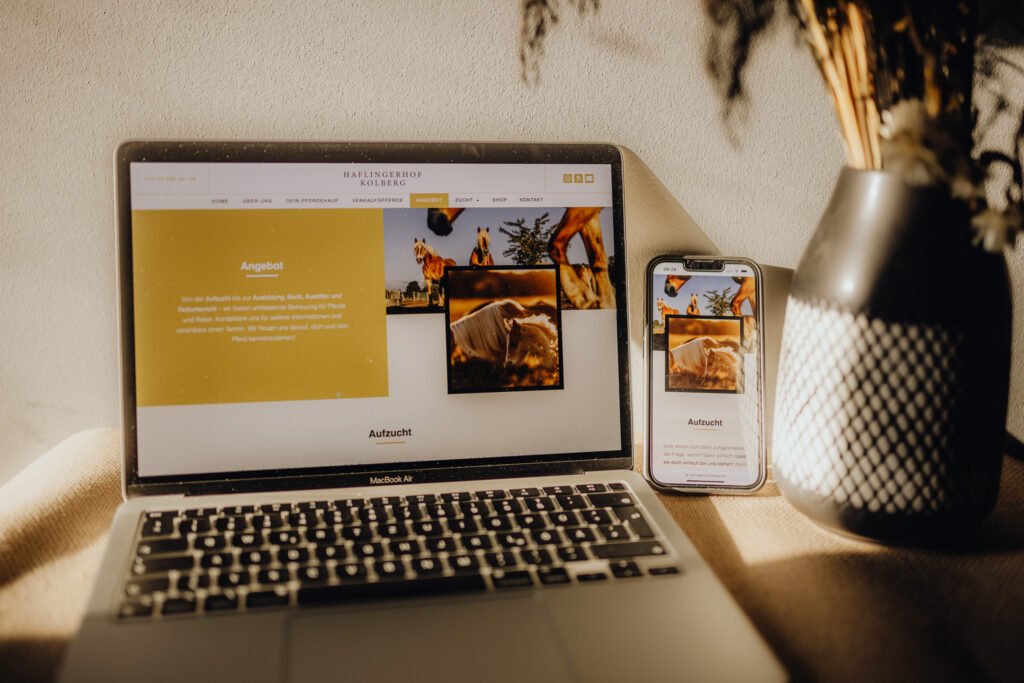 Ein Laptop mit einem Telefon und einer Vase auf einem Tisch.