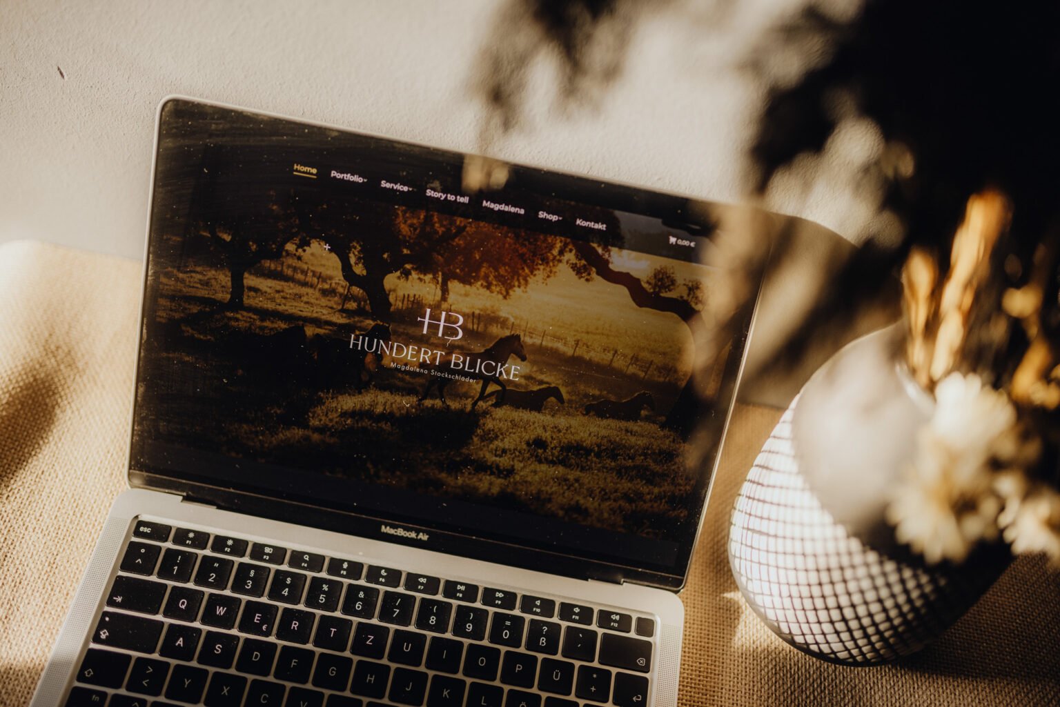 Auf einem Tisch neben einer Vase steht ein Laptop.