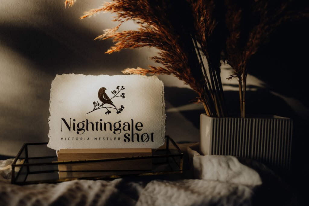 Logodesign "Nightingale Shot" auf einem Tisch neben einer Blumenvase.