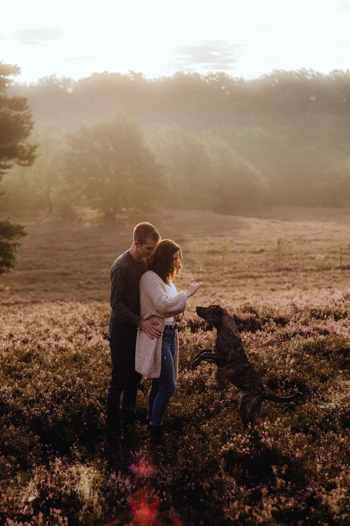 Ein Paar steht mit seinem Hund in der Heide.