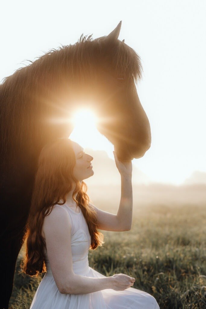 Frau berührt den Kopf ihres Pferdes bei Sonnenaufgang