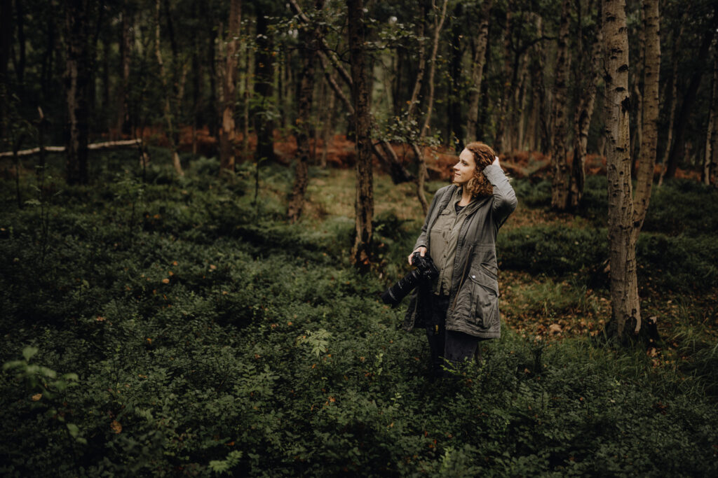 Eine Frau steht mit einer Kamera im Wald.