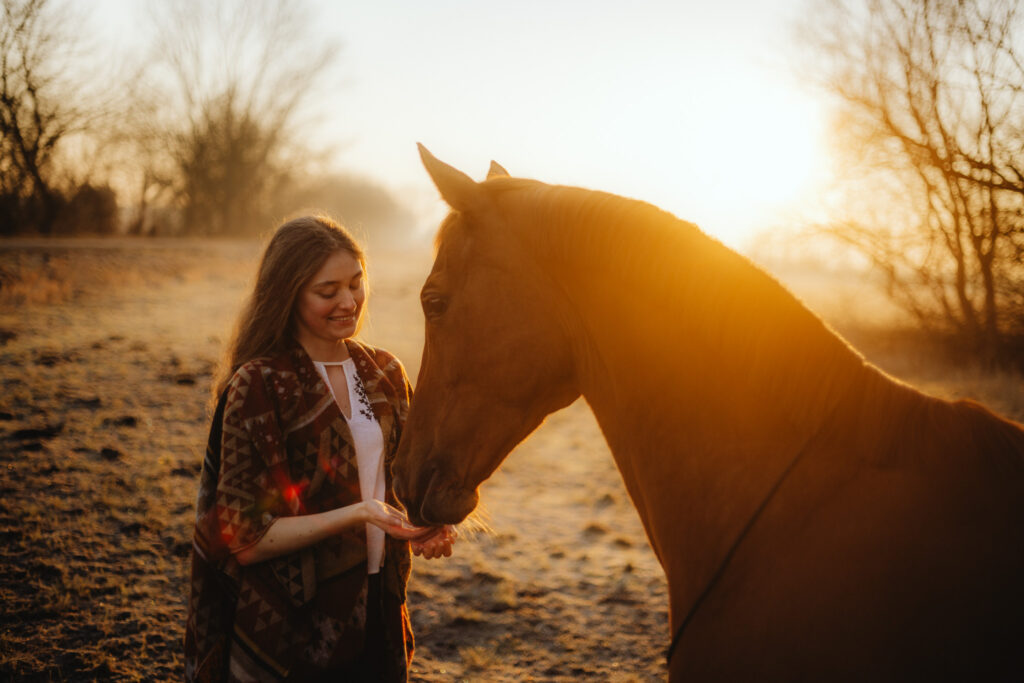 Eine Frau streichelt bei Sonnenaufgang ein Pferd.