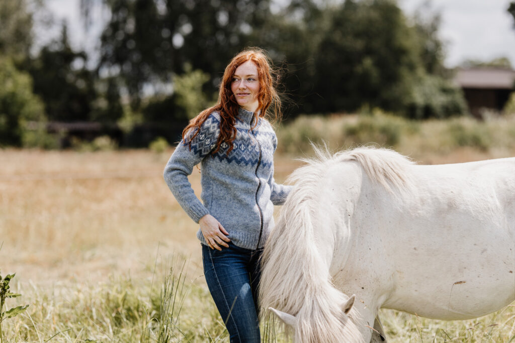Eine Frau steht neben einem weißen Pferd auf einem Feld.